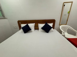 A single bed with a wooden headboard, two pillows, a white chair, and a mirror on the wall. - Namo Krishn Stay Kunj (Mathura)