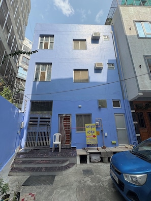 A multi-story building with a blue facade, a visible staircase leading to the entrance, and a parked car in front. - Namo Krishn Stay Kunj (Mathura)