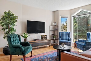 A living room with a large flat-screen TV, a green armchair, a blue plaid armchair, a coffee table, and a large potted plant. - Drop the gloves, then soak it off. A hockey house with a game room (pinball, air hockey & projector), a jacuzzi spa suite & a private backyard with deck, BBQ & fire table. 12 min to River Cree Casino, 14 min to WEM. A weekend your crew won't forget. (Edmonton)