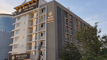 Un immeuble hôtelier à plusieurs étages, doté de balcons et d’une enseigne indiquant « Ruby Suites Hotel Jaipur ».