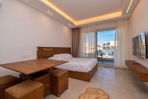 A modern hotel room with a bed, a wooden desk, a television, and a view of the city. - Infinity Pool View Studio at Maraya El Gouna, Red Sea (Hurghada)