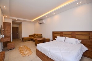 A modern bedroom with a large bed, a sofa, a wooden nightstand, and a wall-mounted air conditioner. - Infinity Pool View Studio at Maraya El Gouna, Red Sea (Hurghada)