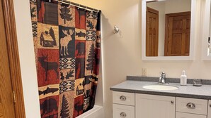 A bathroom with a white vanity, a mirror, a shower curtain with a deer pattern, and a black tiled floor. - Pet-Friendly 6BR Retreat on 14 Acres, Sleeps 12, Near Grand Rapids MN (Grand Rapids)