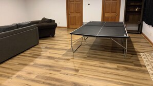 A room with a ping pong table, a sofa, wooden flooring, and two wooden doors. - Pet-Friendly 6BR Retreat on 14 Acres, Sleeps 12, Near Grand Rapids MN (Grand Rapids)