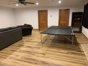 A room with a ping pong table, a sofa, wooden flooring, and two wooden doors. - Pet-Friendly 6BR Retreat on 14 Acres, Sleeps 12, Near Grand Rapids MN (Grand Rapids)
