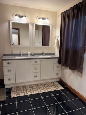 Een badkamer met een dubbele wastafel, twee spiegels, een wasbak en een douchegordijn.