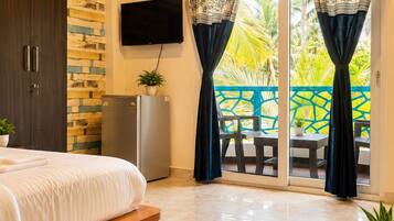 A bedroom with a bed, a TV, a refrigerator, and a balcony with curtains.