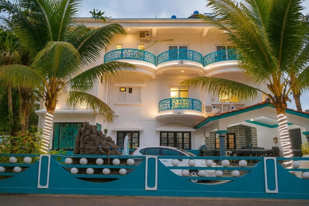 A multi-story building with balconies, a car parked in front, and palm trees.