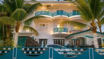 A multi-story building with balconies, a car parked in front, and palm trees.