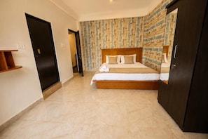 A hotel room with a large bed, a wardrobe, a small shelf, and a patterned wall. - Mogachi Casa Goa Beach Stay (Calangute)