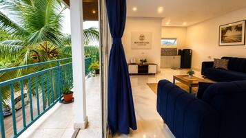 A modern living room with a sofa, a coffee table, and a TV. There is a balcony with a railing and potted plants.