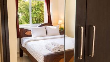 Habitación de hotel con cama, ventana con cortinas, unidad de aire acondicionado y puerta con picaporte.