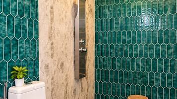 A bathroom with a toilet, a shower, and a green tiled wall.