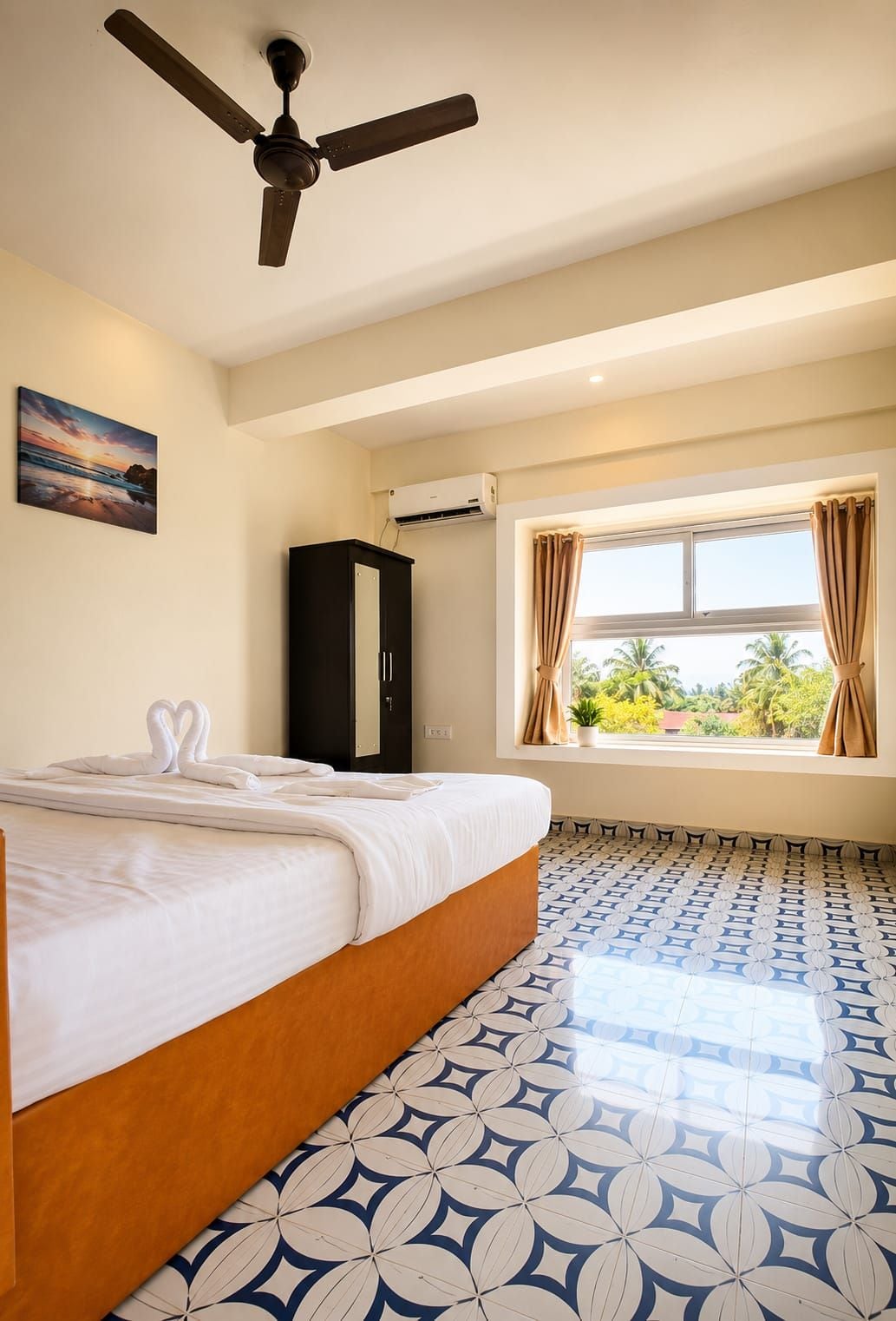 A hotel room with a bed, a ceiling fan, an air conditioning unit, a window with curtains, and a patterned floor.