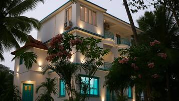 Un edificio de varios pisos con balcón, rodeado de vegetación tropical.