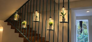 Una escalera con escalones de madera y barandillas color turquesa, flanqueada por plantas en macetas sobre estantes.