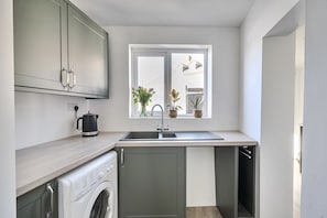 A compact kitchen with a washing machine, a sink, and cabinets. - 10 Riverside 3‑bed cosy family home sleeps 6 Nr beach (Sidmouth)