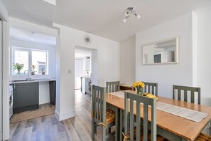 A modern kitchen with a built-in dishwasher, a dining area with a wooden table and chairs, and a large mirror on the wall. - 10 Riverside 3‑bed cosy family home sleeps 6 Nr beach (Sidmouth)