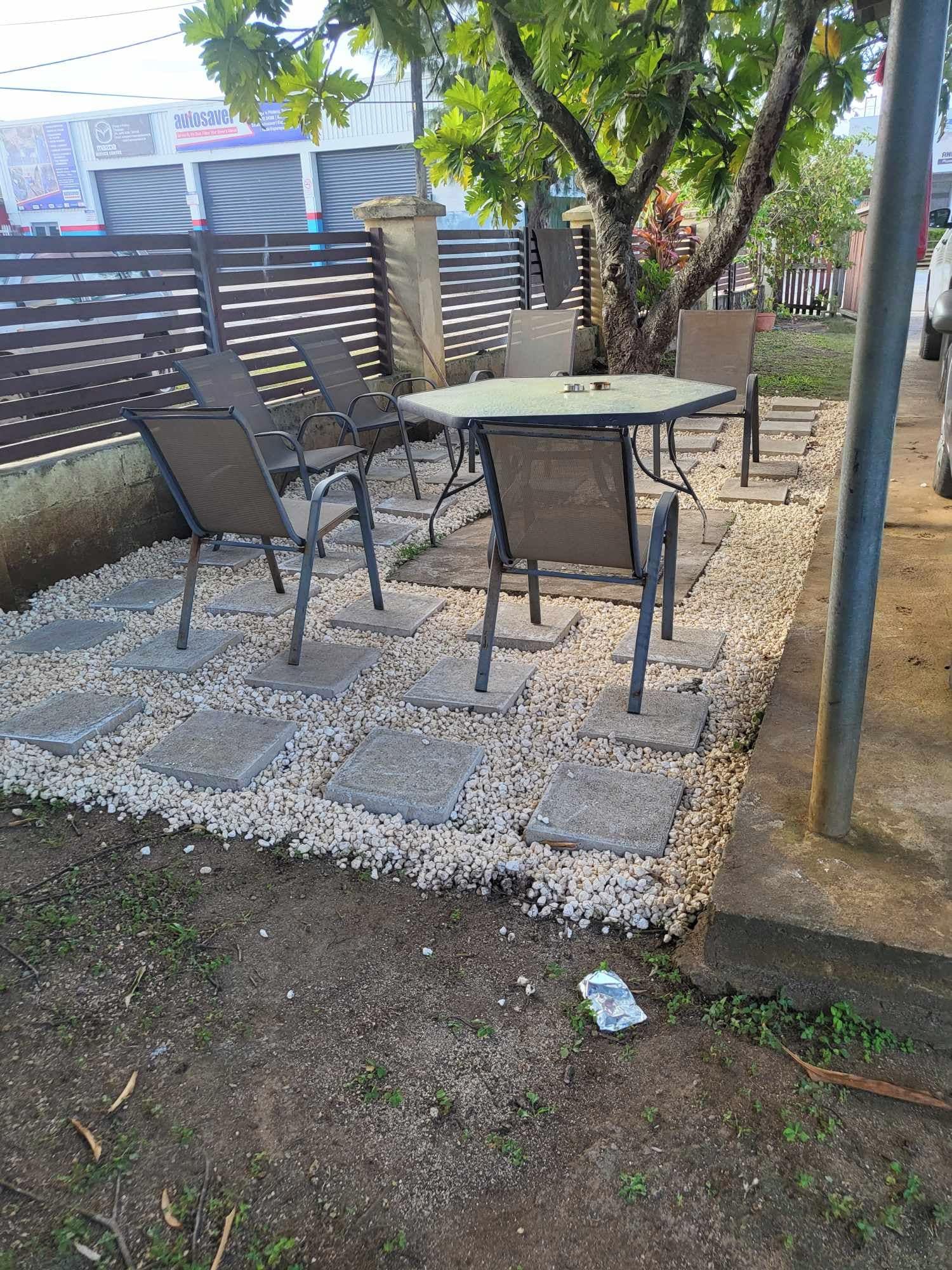 Un espace extérieur aménagé en terrasse, avec une table et des chaises, entouré d’une bordure de gravier et d’une clôture en métal.