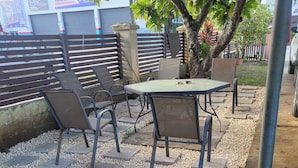 Ein möblierter Patio-Bereich mit Tisch und Stühlen, umgeben von einem Kiesstreifen und einem Metallzaun.