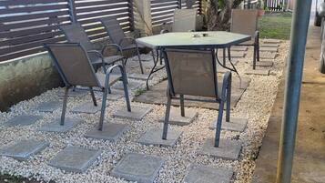 An outdoor patio area with a table and chairs, surrounded by a gravel border and a metal fence.