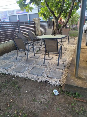 Ein möblierter Patio-Bereich mit Tisch und Stühlen, umgeben von einem Kiesstreifen und einem Metallzaun.