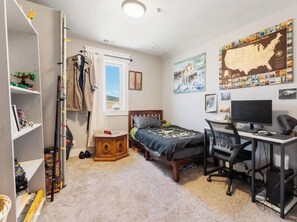 A bedroom with a bed, desk, computer, and shelves.