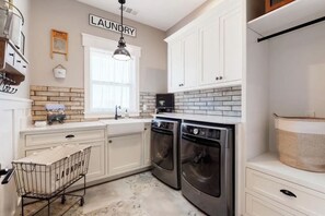 A kitchen with white cabinets, a brick backsplash, a washing machine, and a laundry cart.