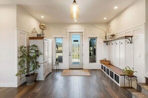 A hallway with a wooden floor, white walls, a door with glass panels, and a hanging light fixture.