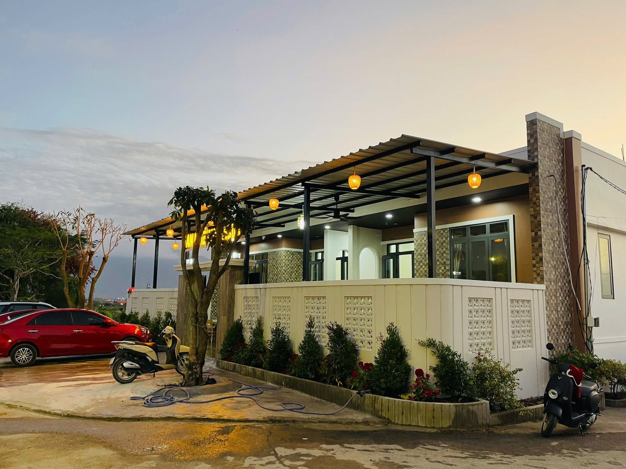 A building with a covered outdoor area, a cross, and a parking lot with cars and scooters.