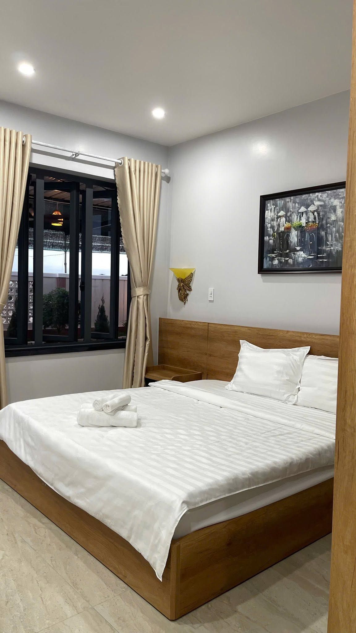 Ein Hotelzimmer mit Bett, Vorhängen, einer Wandleuchte und einem Gemälde.