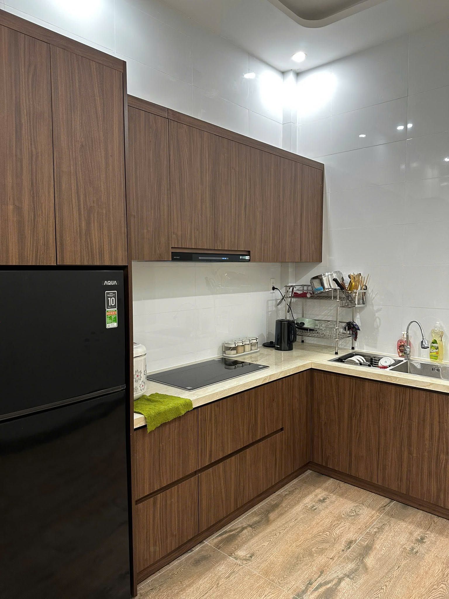 Une cuisine moderne avec des meubles en bois, un réfrigérateur noir et un évier en acier inoxydable.
