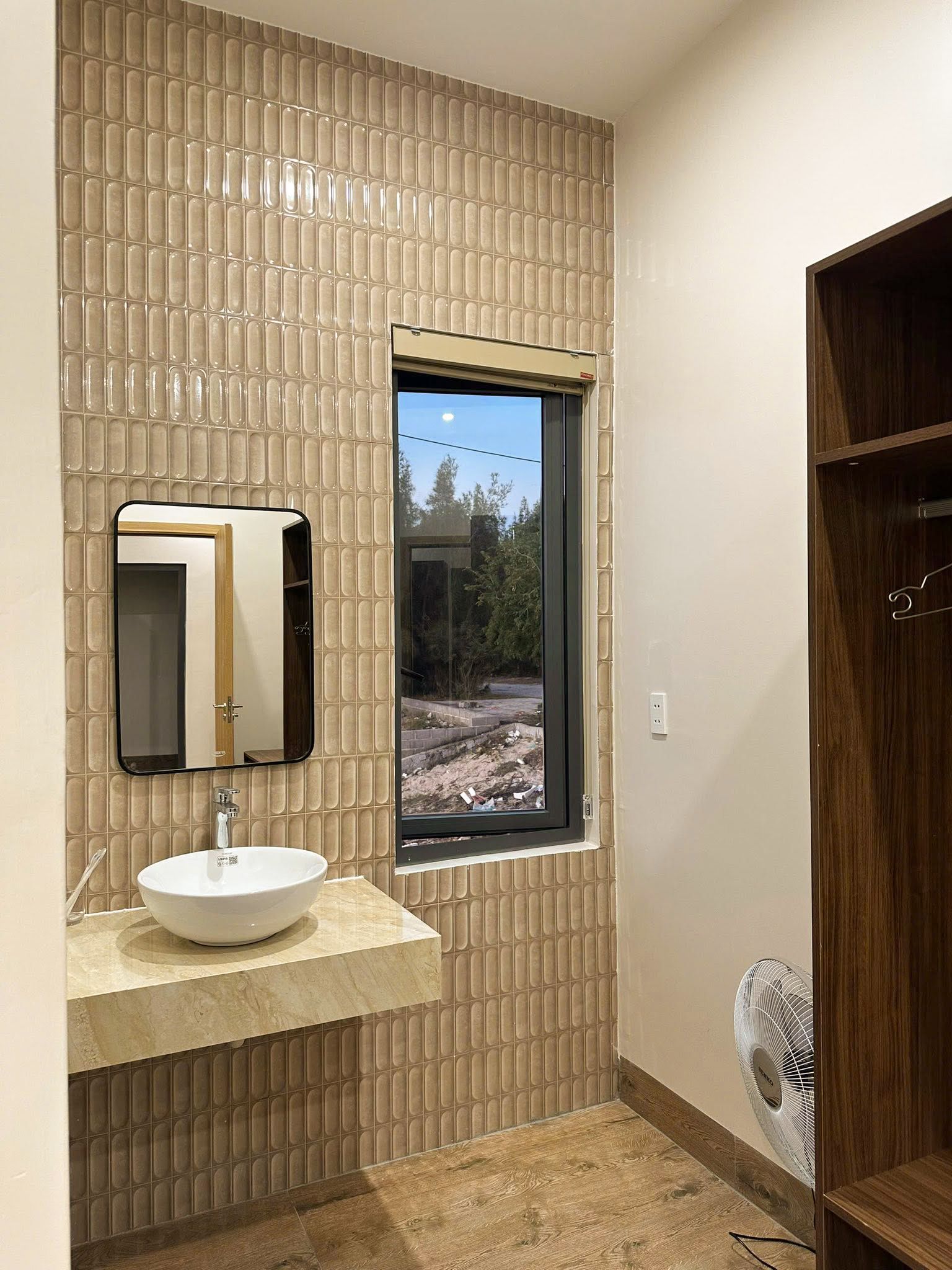 A bathroom with a large window, a sink with a mirror, and a wooden cabinet.