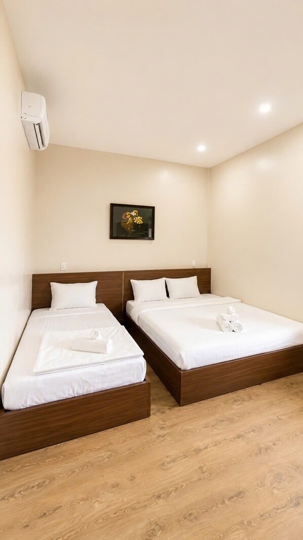 Habitación de hotel con dos camas individuales, un cabecero de madera, un pequeño cuadro en la pared y un equipo de aire acondicionado.