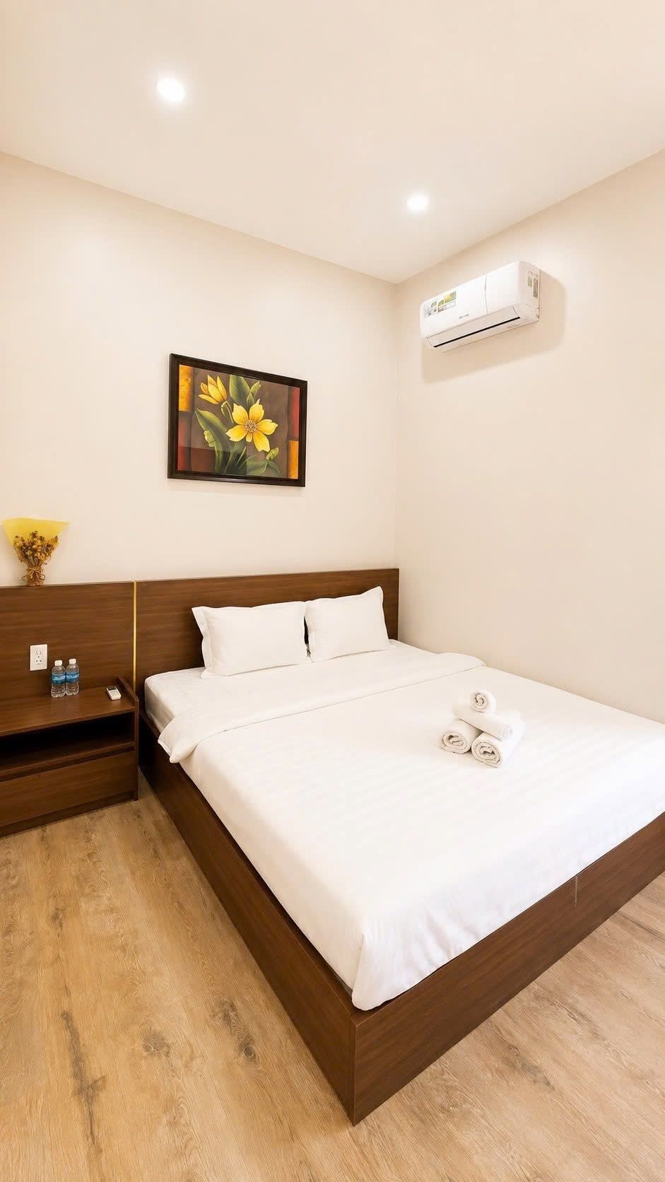 Una habitación de hotel con una cama, una mesita de noche, un aire acondicionado de pared y un cuadro.