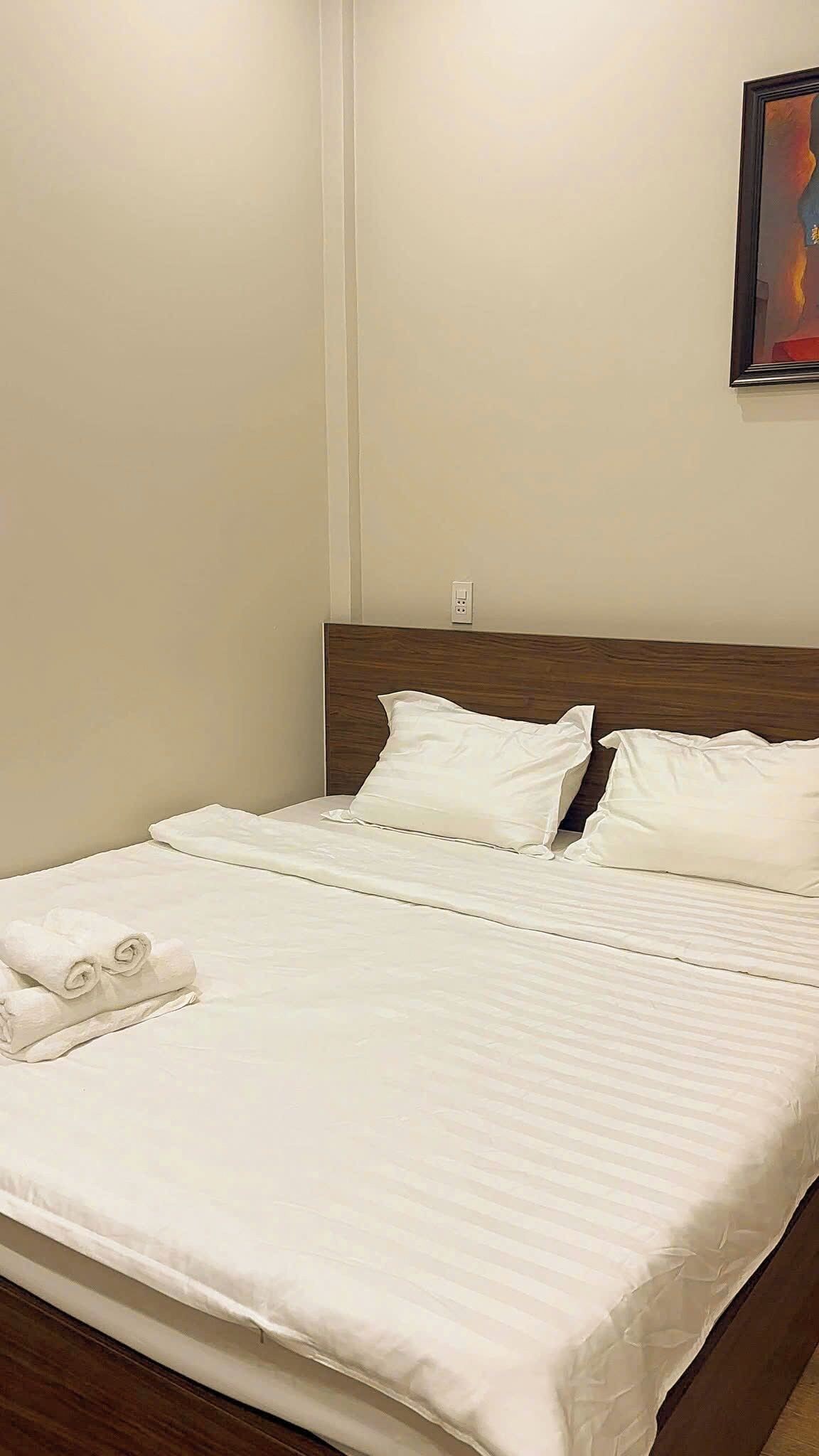 Cama bem arrumada com roupa de cama branca e cabeceira de madeira em quarto de hotel.