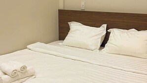 Una cama bien hecha con sábanas blancas y un cabecero de madera en una habitación de hotel.