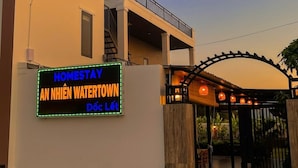A hotel entrance with a neon sign, a covered walkway, and a gated entrance. - Anna Home Doc Let (Dong Ninh Hoa)