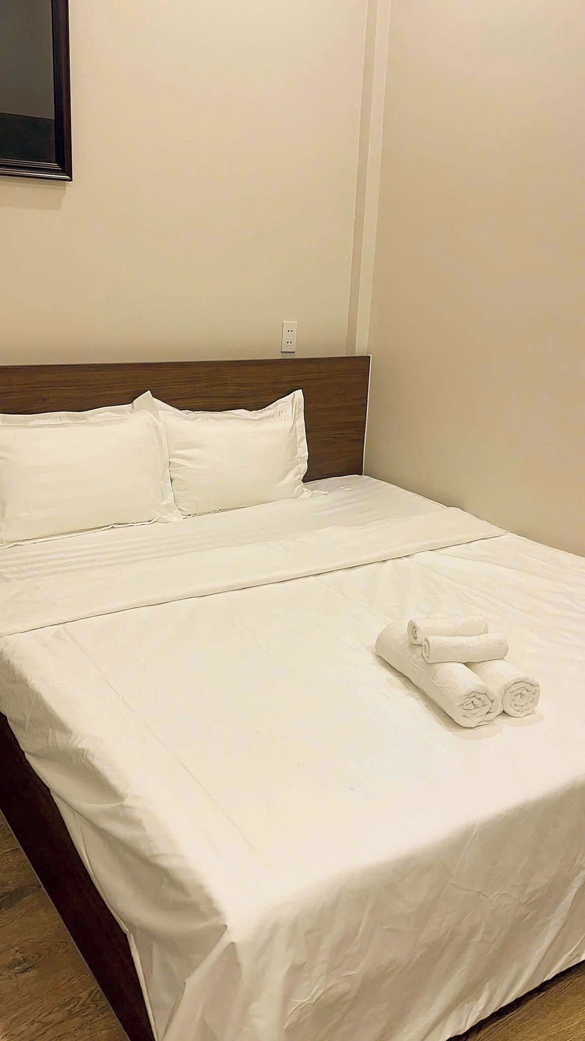 A neatly made bed with white linens and two rolled towels on the footboard.