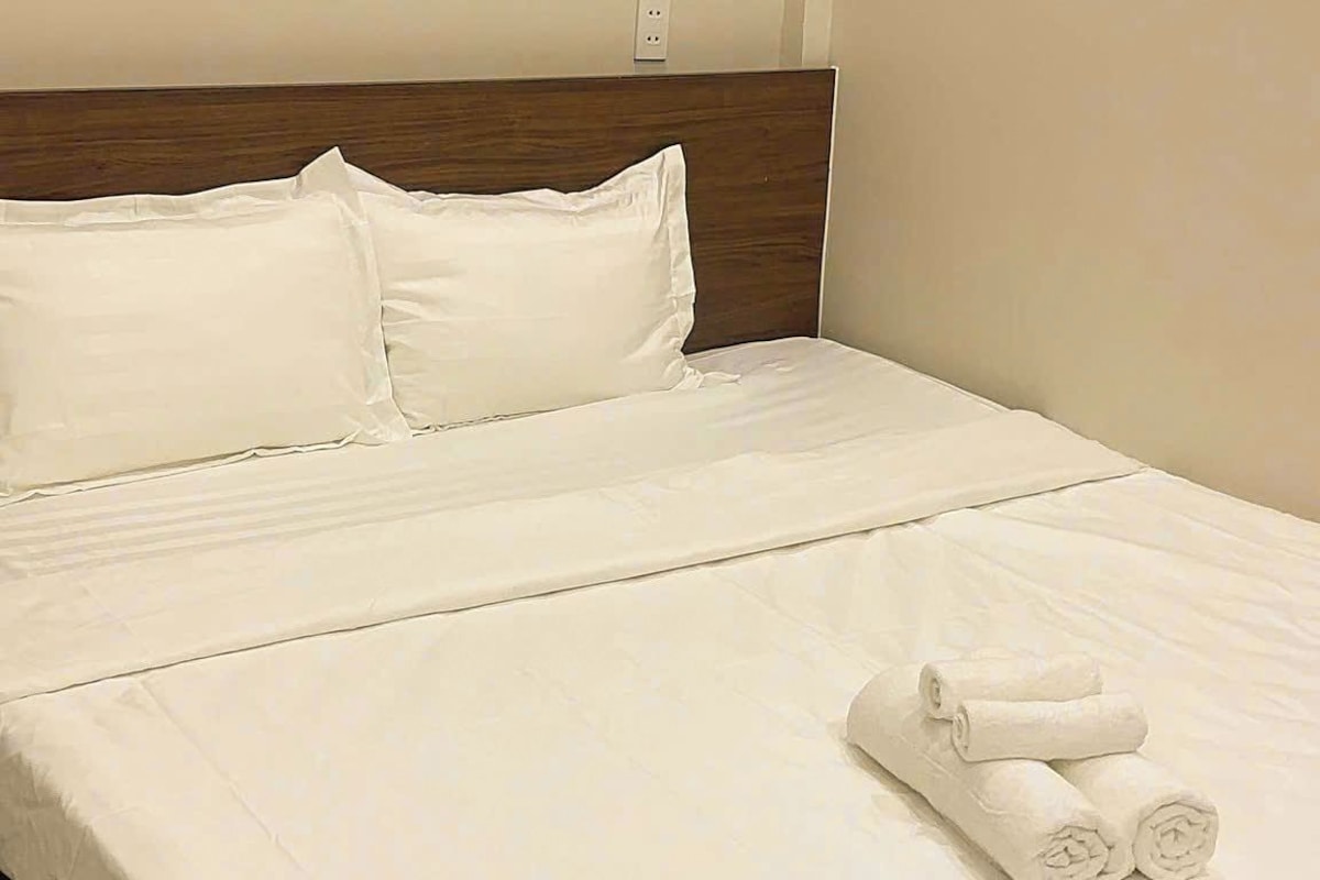 Ein ordentlich bezogenes Bett mit weißen Leinen und zwei aufgerollten Handtüchern am Fußteil.