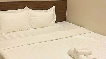 A neatly made bed with white linens and two rolled towels on the footboard.
