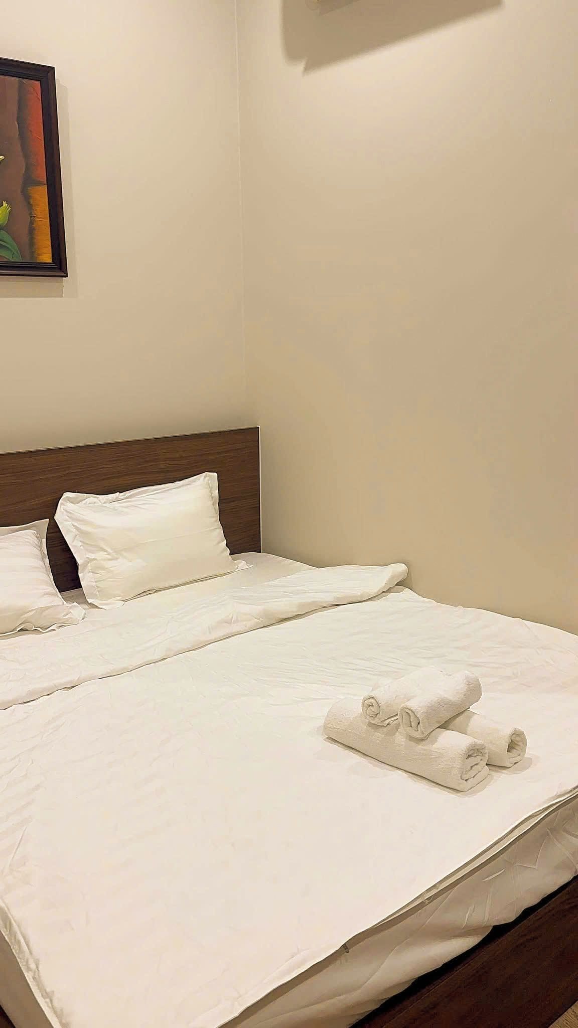 Cama bem arrumada com lençóis brancos e uma toalha enrolada ao lado.