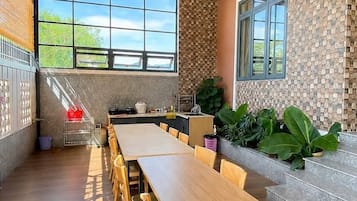 Un comedor amplio con una larga mesa de madera y sillas, un ventilador de techo y ventanas grandes que dejan entrar luz natural.