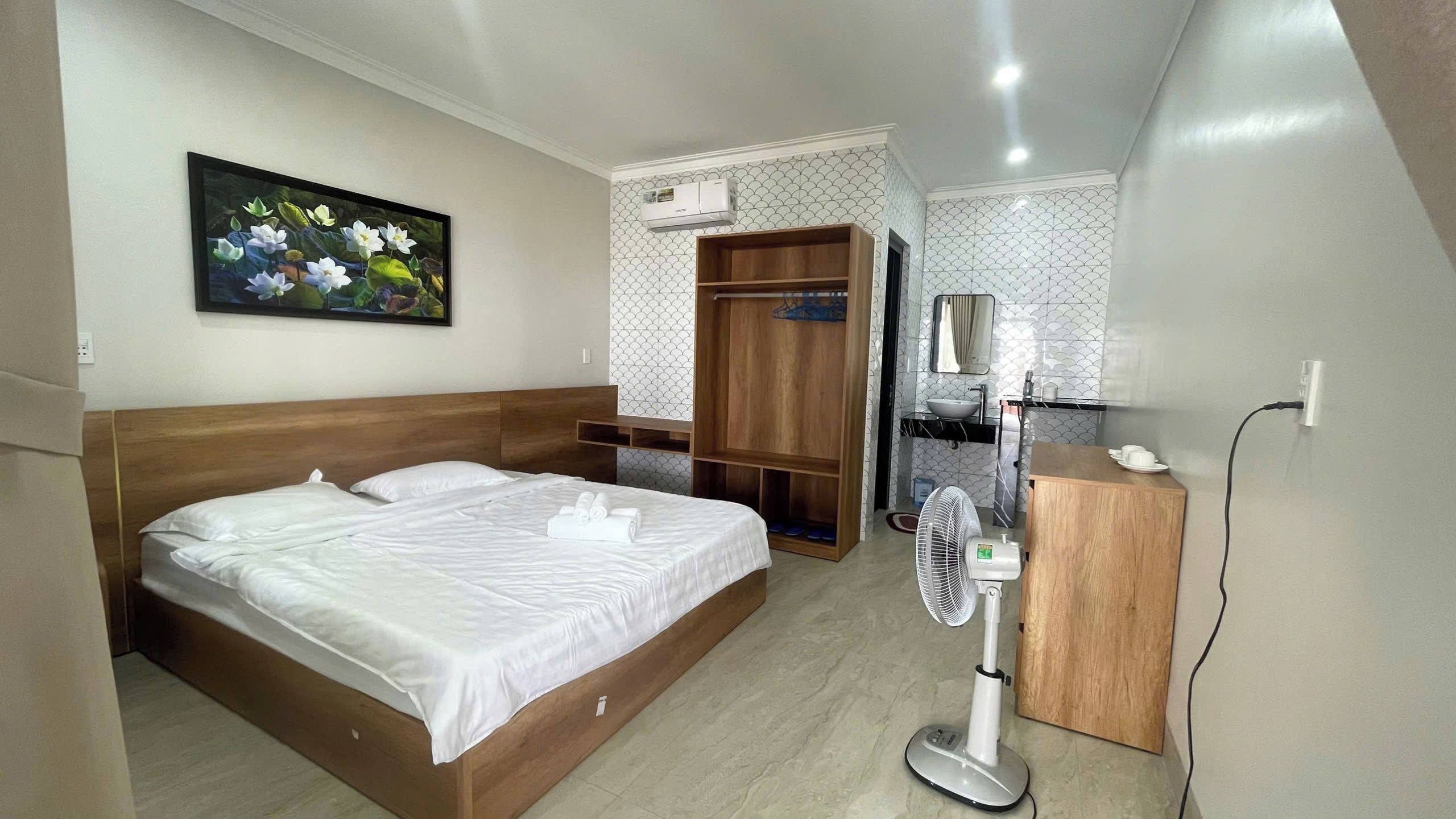 A hotel room with a bed, a bedside table, a mirror, a wardrobe, and a bathroom with a sink and a fan.