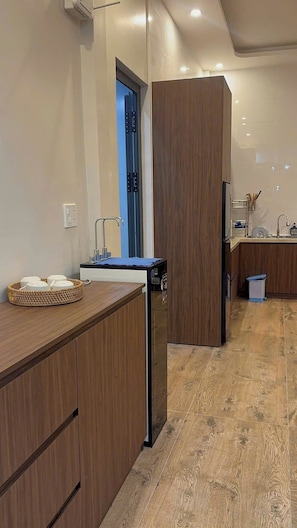 A modern kitchen with wooden cabinetry, a built-in dishwasher, and a small sink. - Anna Home Doc Let (Dong Ninh Hoa)