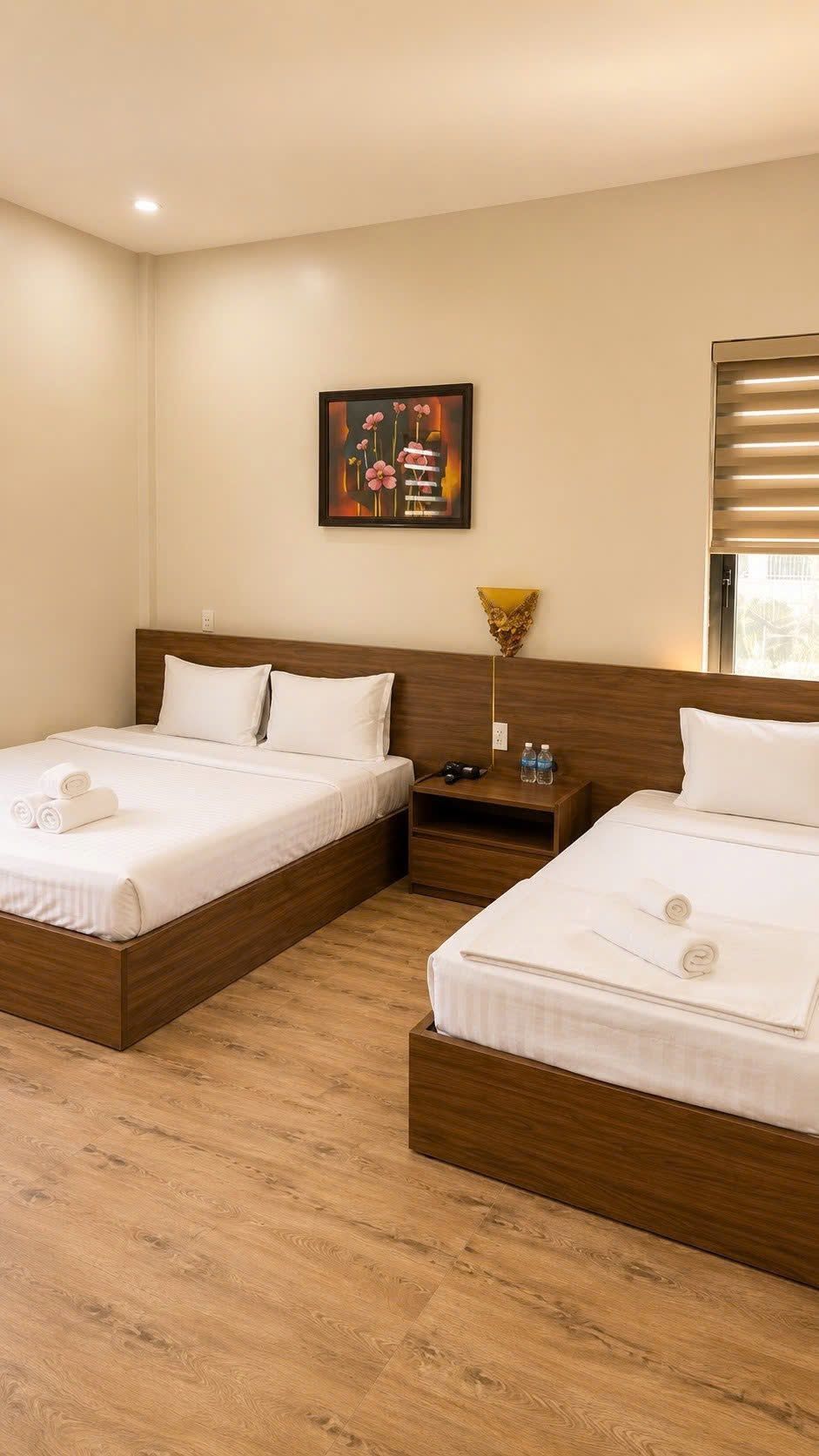 Une chambre d’hôtel avec deux lits, une table de chevet, une lampe fixée au mur et un tableau encadré.