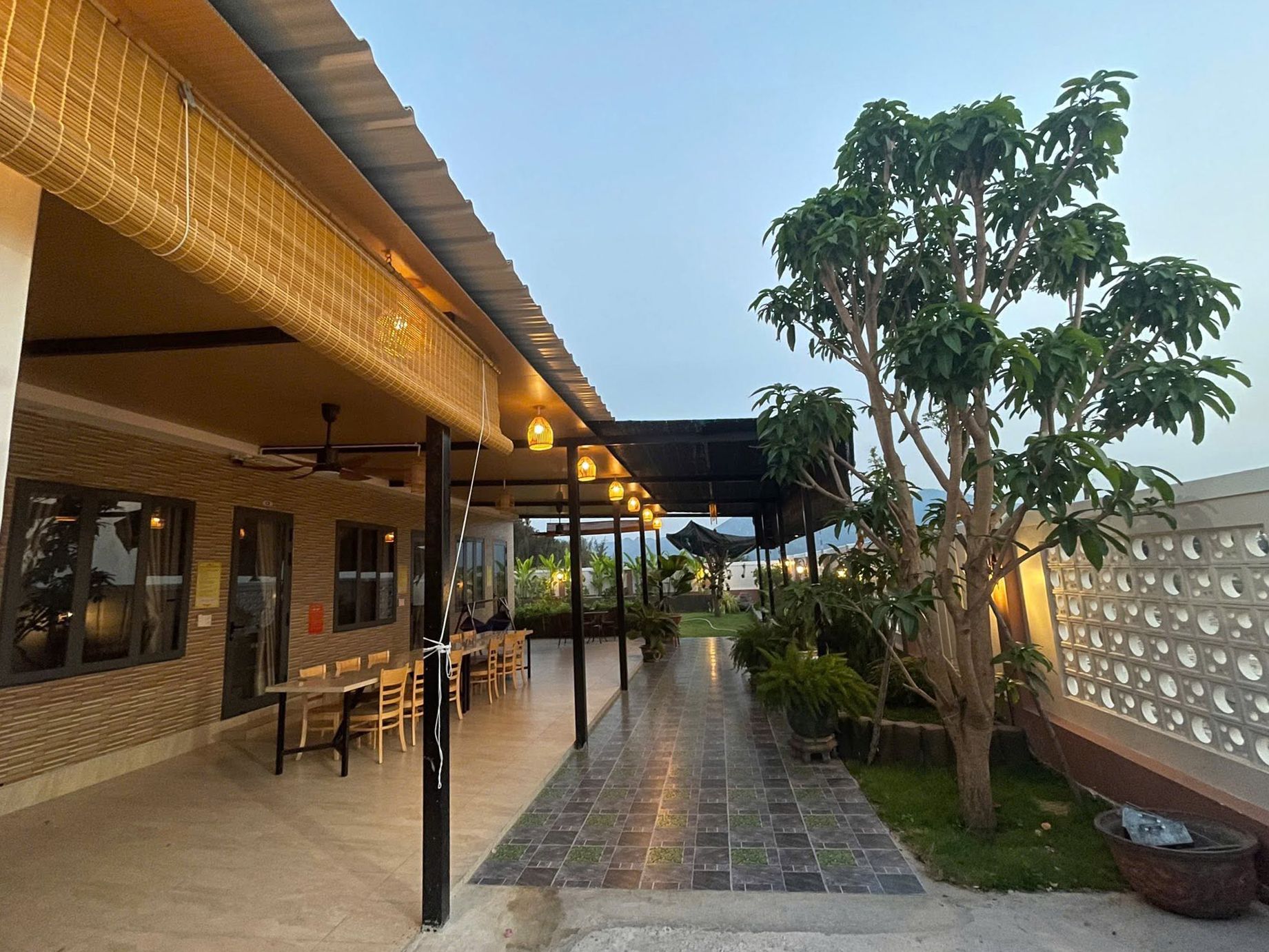 An outdoor seating area with tables and chairs, a covered walkway, and a large tree.