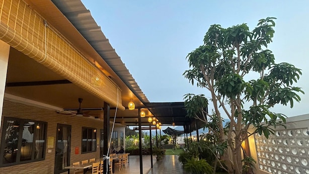 An outdoor seating area with tables and chairs, a covered walkway, and a large tree. - Anna Home Doc Let (Dong Ninh Hoa)