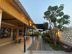 Un espacio al aire libre con mesas y sillas, un paseo techado y un árbol grande.