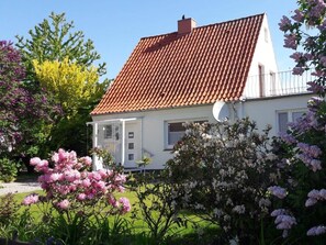 Ein Haus mit rotem Ziegeldach, weißer Fassade und einem Garten mit rosa Blüten.